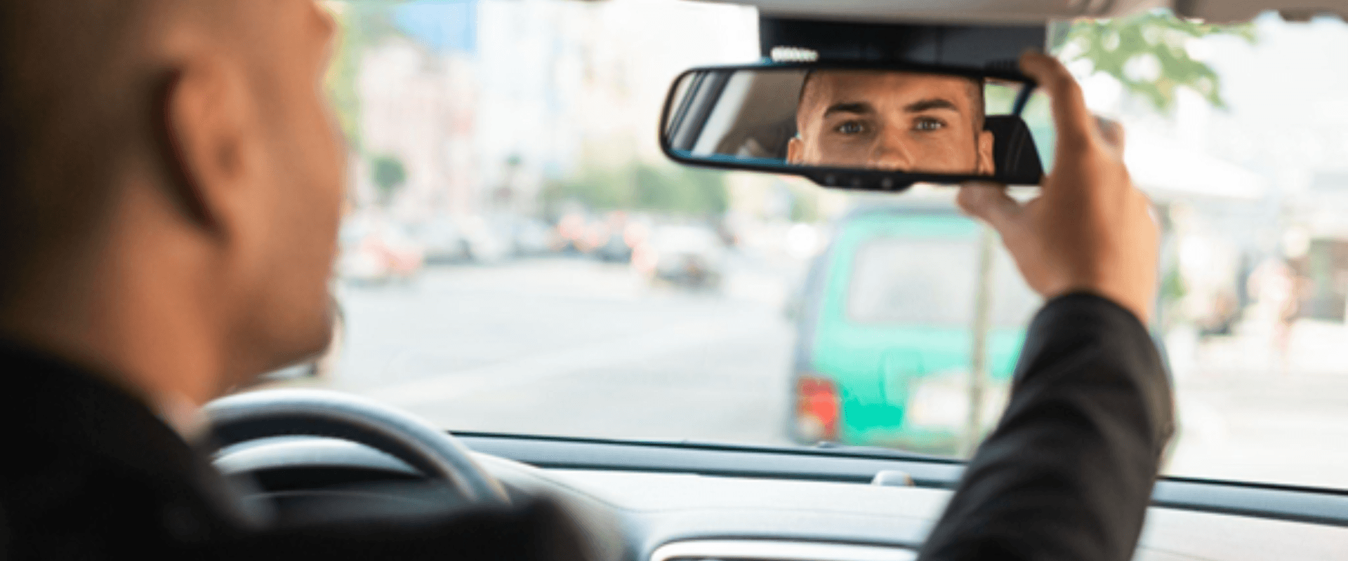 Homem dentro de um carro olhando no espelho retrovisor interno.