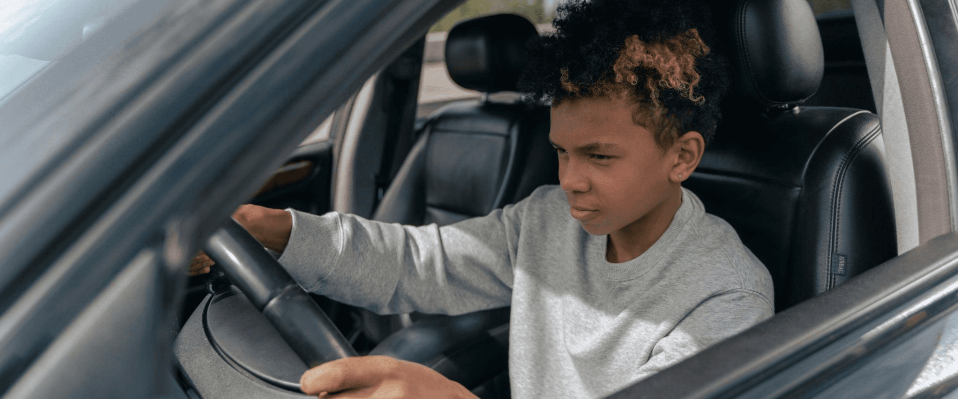 Jovem garoto concentrado ao volante de um carro, dirigindo com atenção e segurança no trânsito.