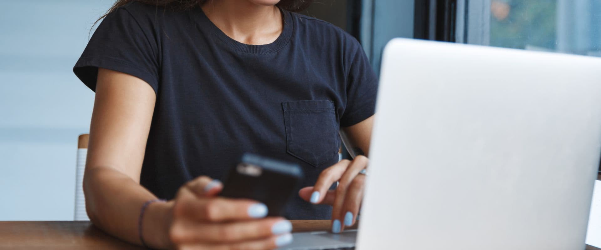 Pessoa usando celular e laptop, focada em atividades digitais em ambiente interno