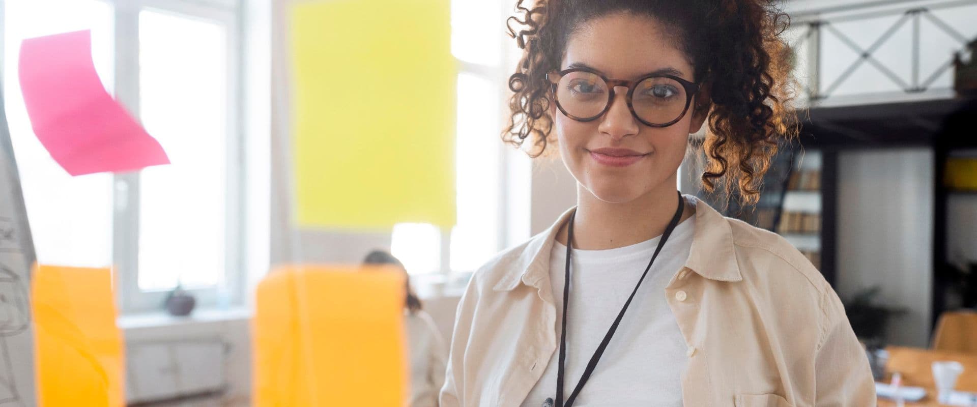 ovem mulher de óculos com cabelo cacheado em ambiente de escritório moderno, sorrindo e transmitindo confiança, ideal para conteúdo de tecnologia e inovação.