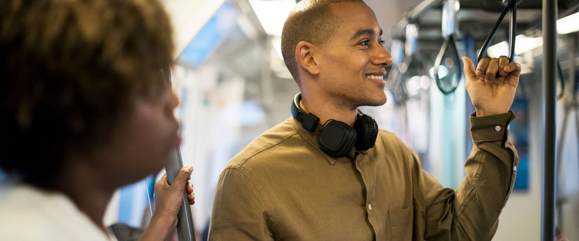 Homem sorridente usando um metrô, com fone de ouvido no pescoço, no transporte público, representando a importância do transporte público no dia a dia.