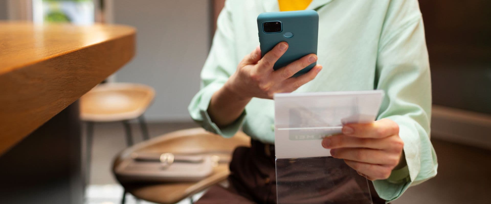 Pessoa usando smartphone e leitura de documento em ambiente moderno, foco na comunicação digital e tecnologia móvel para negócios ou lazer.