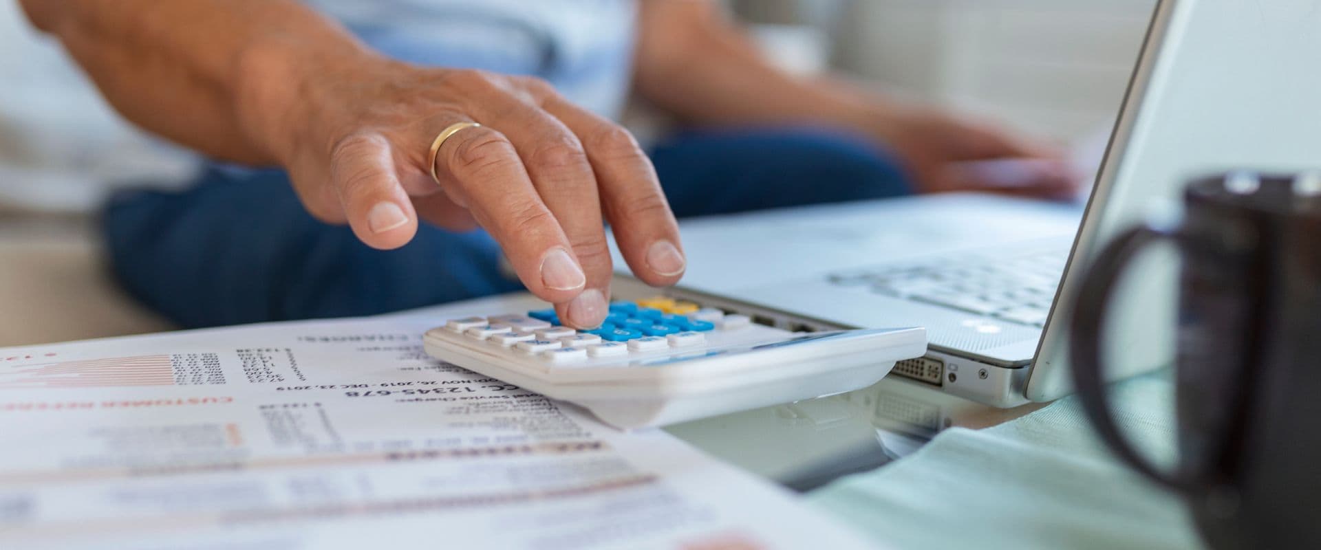 Pessoa usando calculadora para finanças ou contabilidade, com documentos e laptop na mesa, rotina de trabalho ou estudo financeiro.