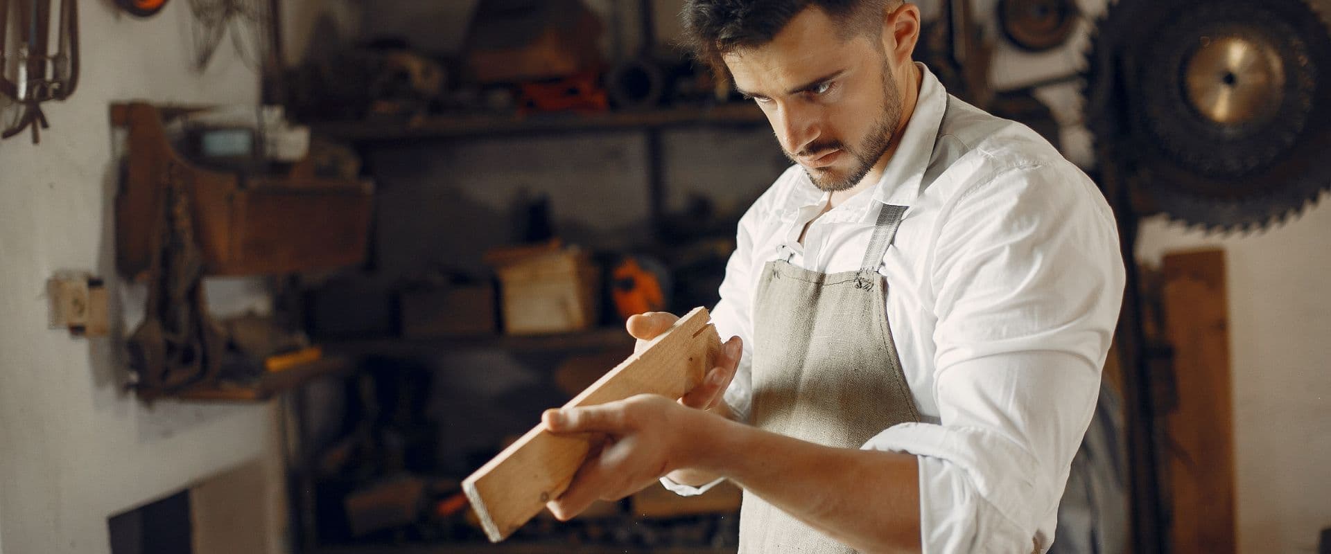 Homem trabalhando com madeira em uma oficina de carpintaria, focado em sua tarefa de acabamento em uma peça de madeira artesanal, ambiente bem equipado.