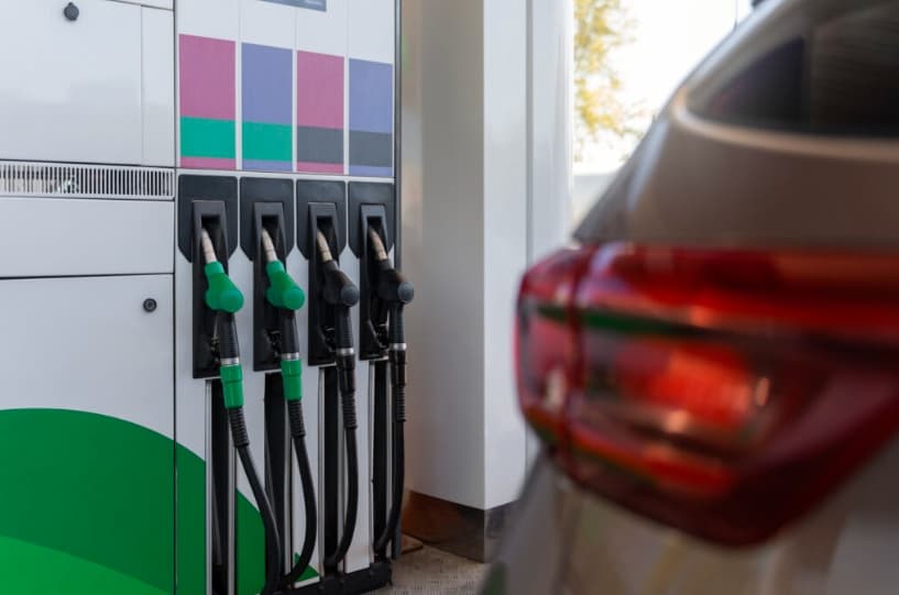 Bomba de combustível em um posto de gasolina, com várias opções de abastecimento visíveis, ao fundo um carro estacionado pronto para abastecer.