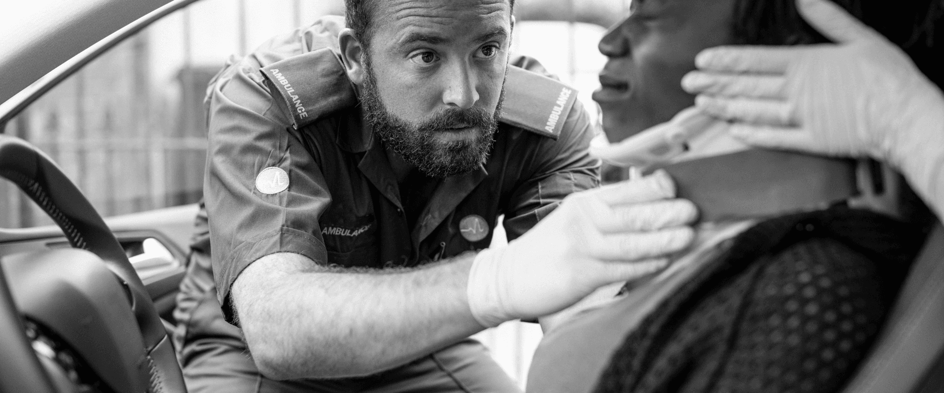 Profissional de saúde realizando atendimento de emergência dentro do carro, concentrado e cuidadoso na assistência médica, com equipamento de suporte à vida ao lado.