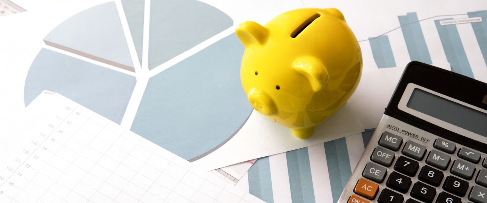 Imagem de um porquinho piggy bank amarelo posicionada ao lado de gráficos e uma calculadora, representando planejamento financeiro e economia.
