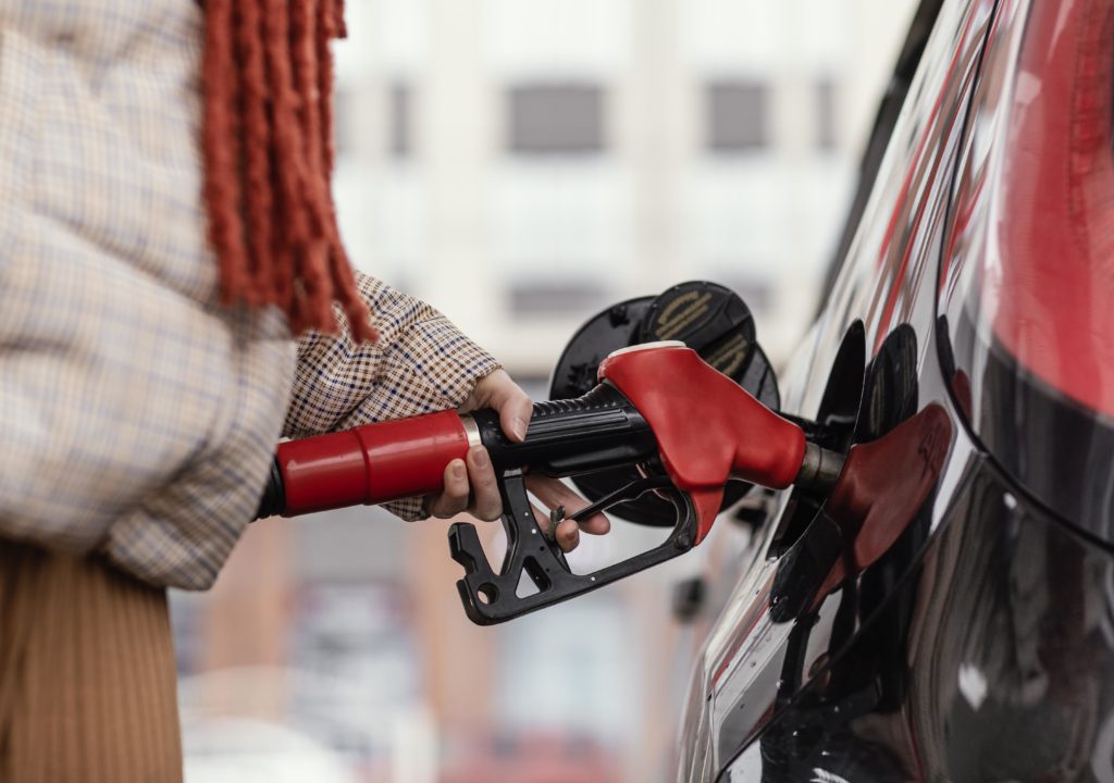 Mulher abastecendo um carro preto com uma mangueira de combustível vermelha.