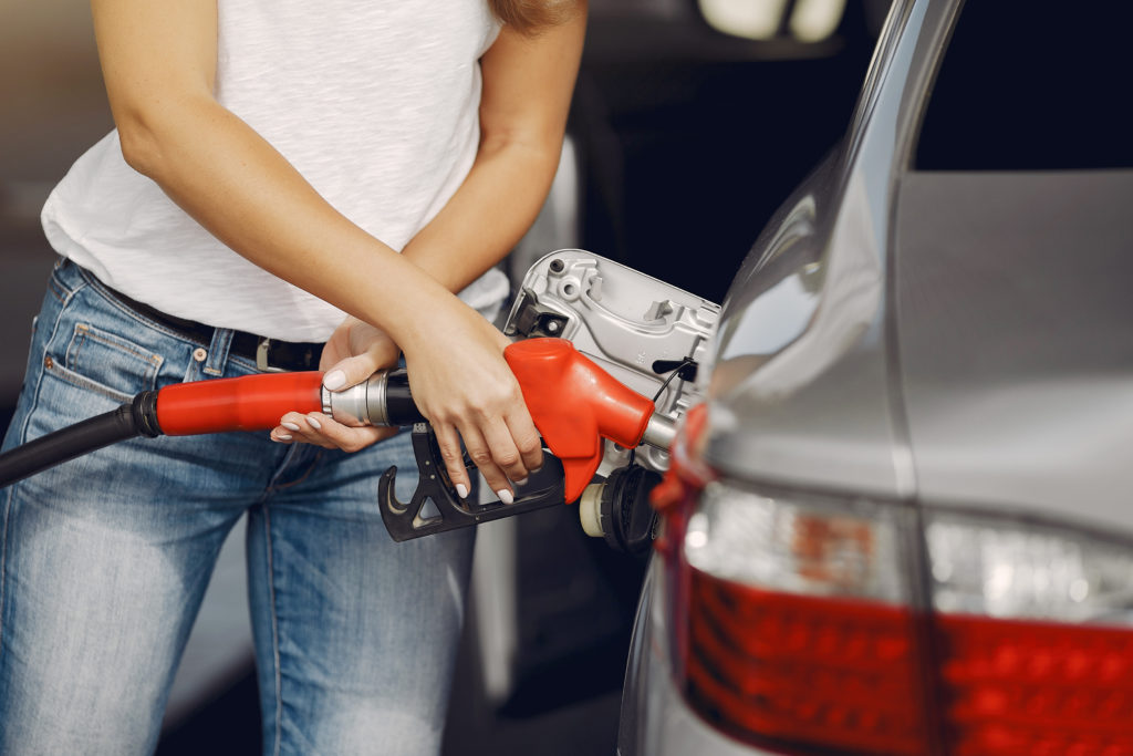 Mulher abastecendo seu veículo prata com uma mangueira de combustível vermelha.