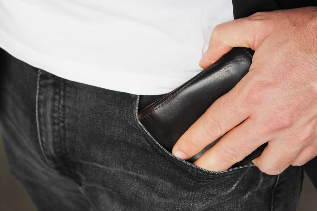 Na imagem há uma pessoa guardando a carteira no bolso da calça.