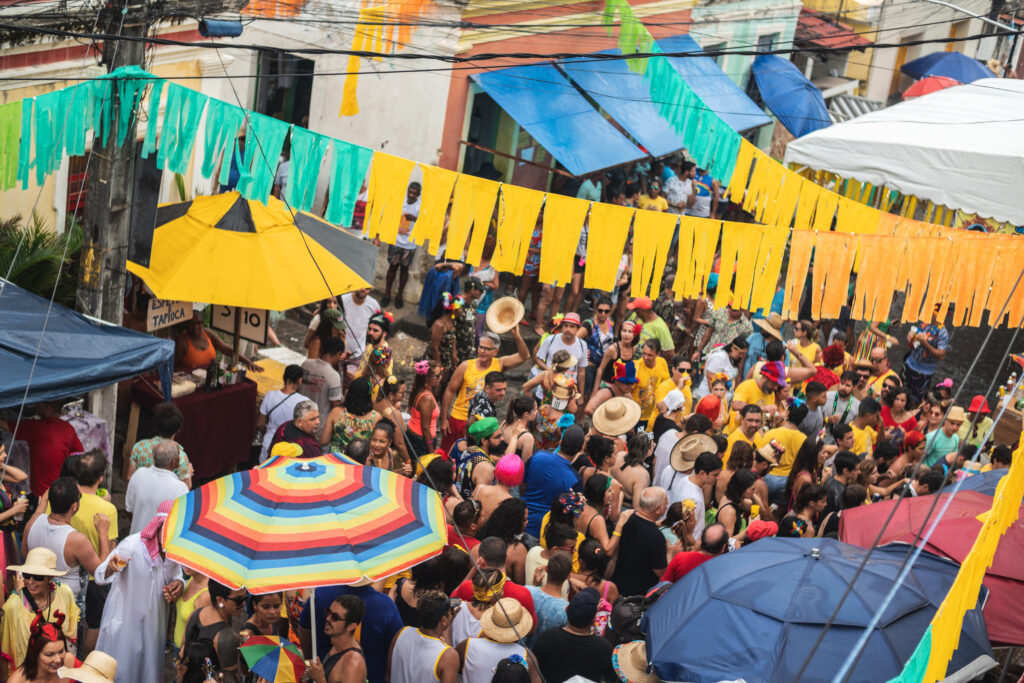 Na imagem há uma rua com muitos foliões que estão aproveitando o feriado de carnaval.