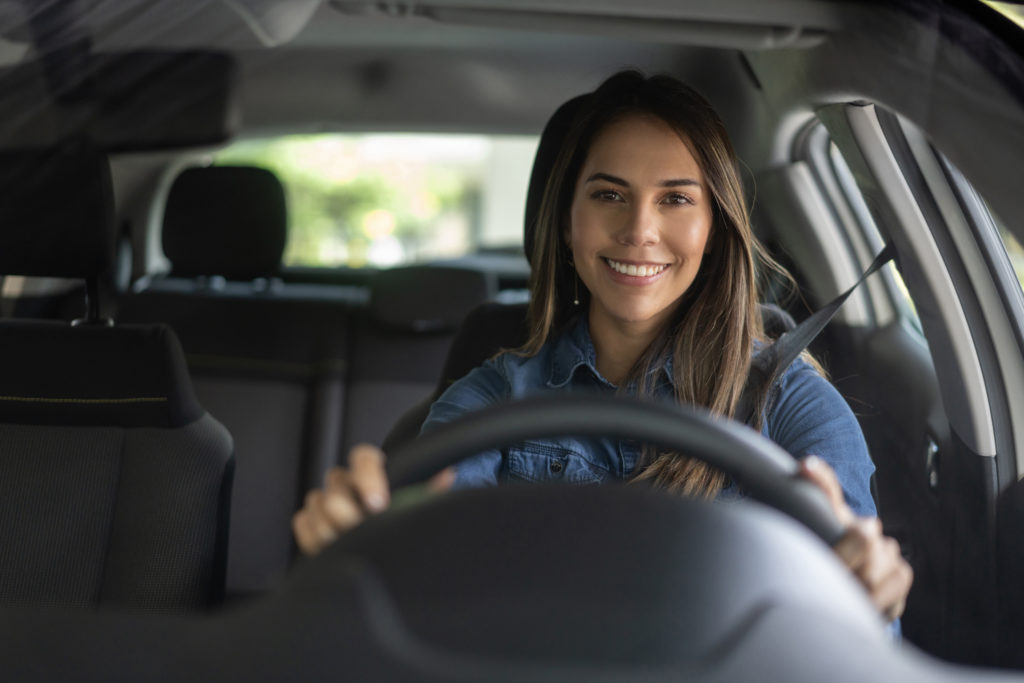 Na imagem há uma mulher sorrindo enquanto dirige um carro automático.