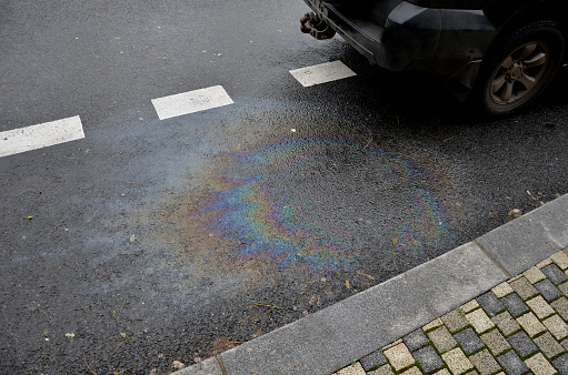 Na imagem há uma poça de óleo em um asfalto.