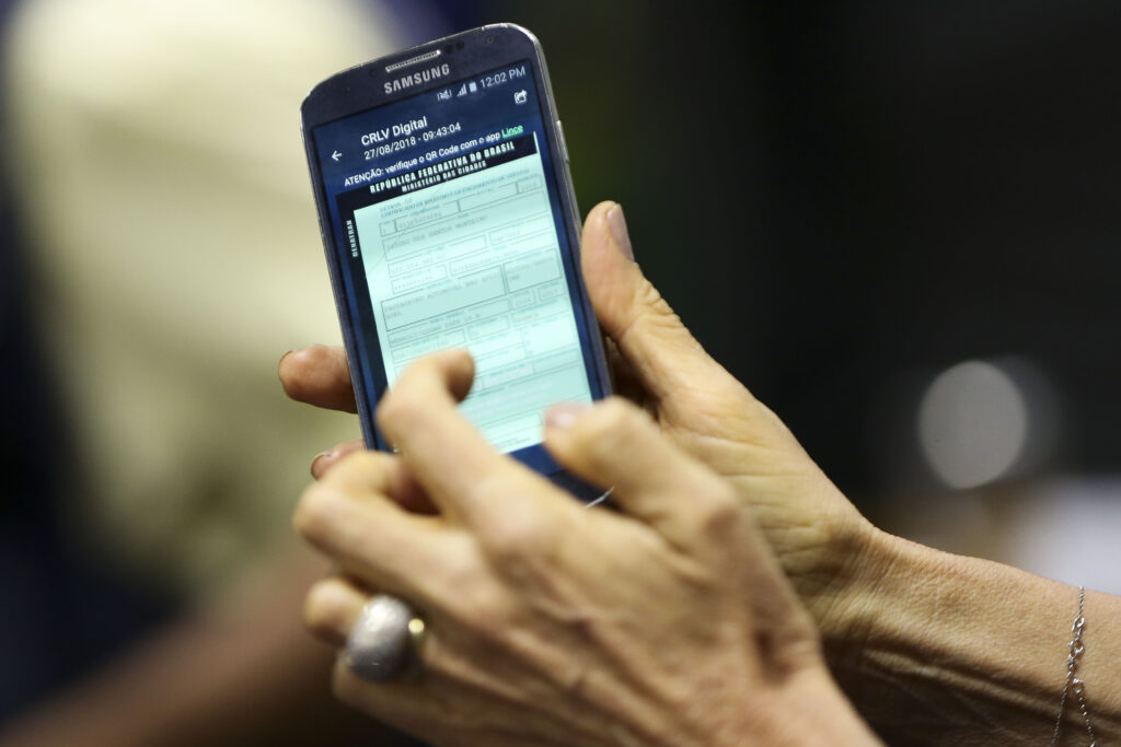 Na imagem há uma pessoa segurando um smarthphone e está sendo exibido um licenciamento digital.